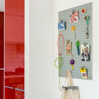 A wall pegboard next to a glossy red kitchen with photographs and scissors hanging from it