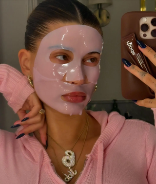 Hailey Bieber wearing a pink face mask and pink sweater with two diamond necklaces