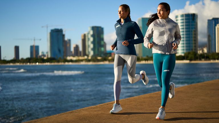 best women's running shoes: Two female athletes running on a sea front wearing the Hoka Arahi 6 shoes