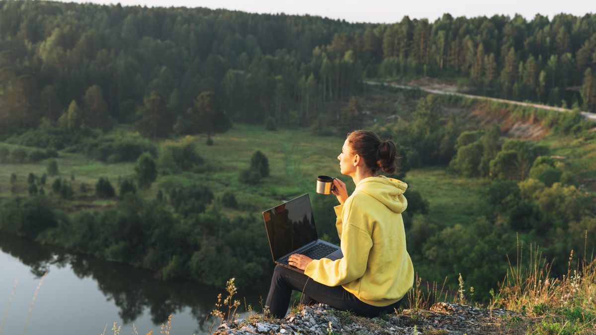 A woman working on the edge of a cliff overlooking a beautiful lake