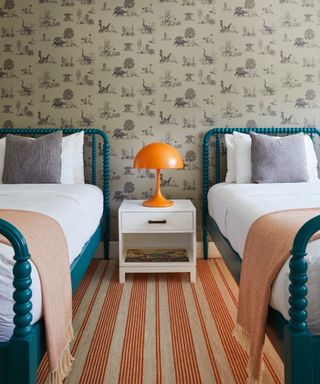 how to make a bedroom darker, twin guest bedrooms/kids bedroom with matching beds and bedding, red stripe rug, orange table lamp, dinosaur wallpaper