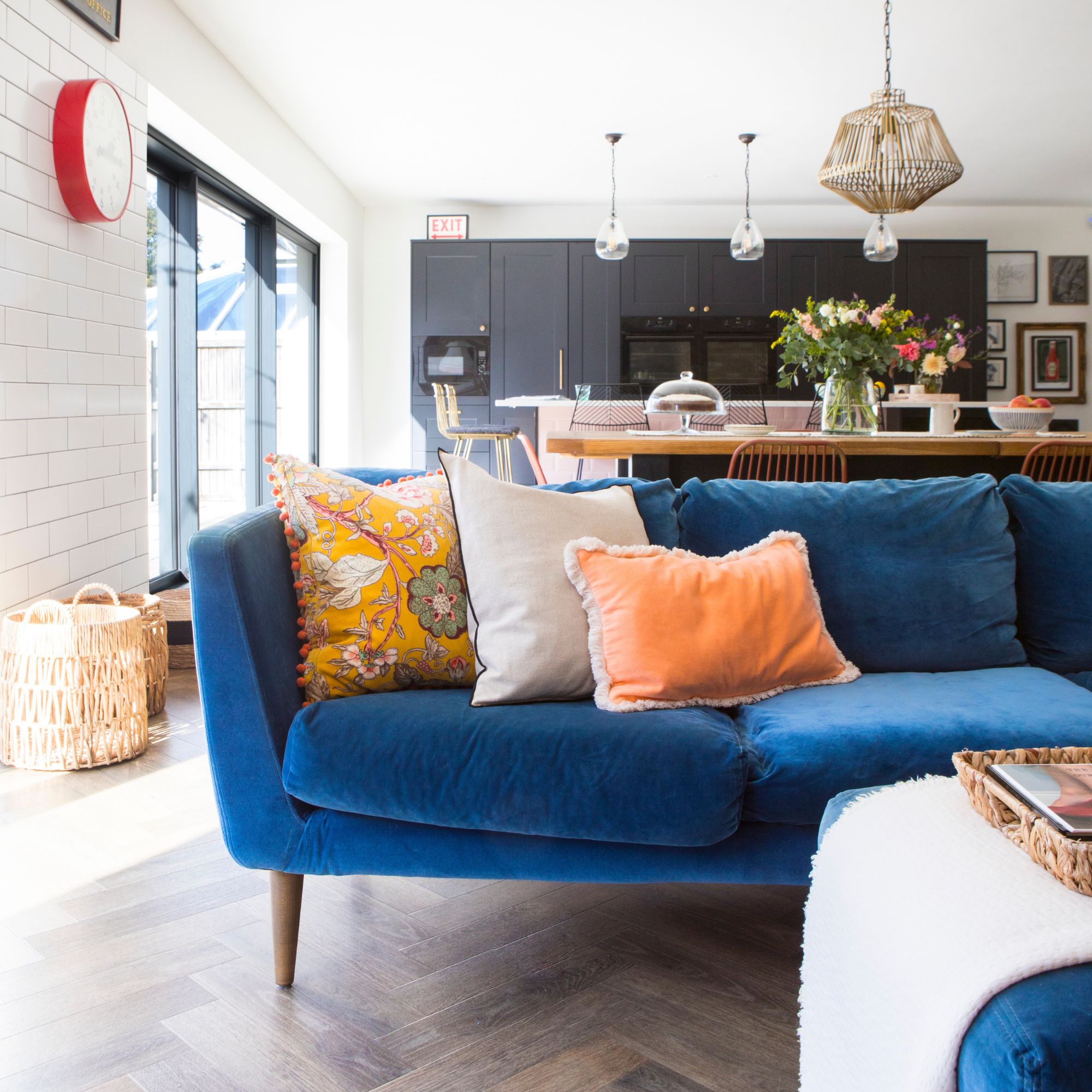 Open plan kitchen and living room with wooden floor and a blue sofa, and a black kitchen behind it