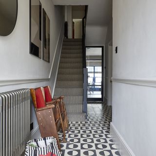 Narrow hallway with black and white tiled floors and a striped stair carpet.