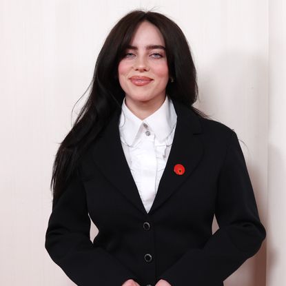 Billie Eilish wearing a white button up shirt and black blazer with red pin