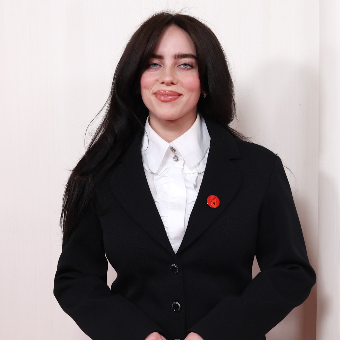 Billie Eilish wearing a white button up shirt and black blazer with red pin