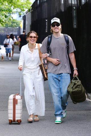 Millie Bobby Brown wears a white collared shirt with white pants and Birkenstock sandals