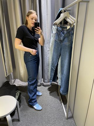 Woman in dressing room wears black t-shirt, blue jeans and blue trainers