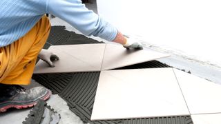 Floor tiles being laid on top of dark tile adhesive