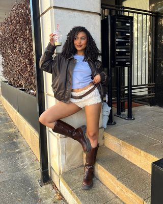 Woman wearing mini ruffled shorts with leather jacket and tall brown boots.