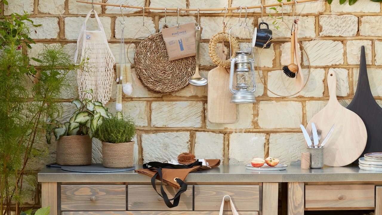 Outdoor kitchen against brick wall with hanging utensils and potted herbs 