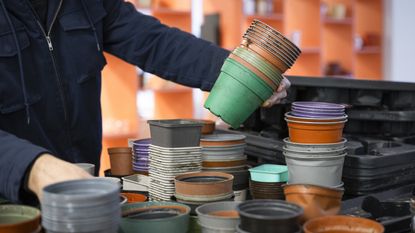 A person lifts a stack of plastic planters from a table covered in them