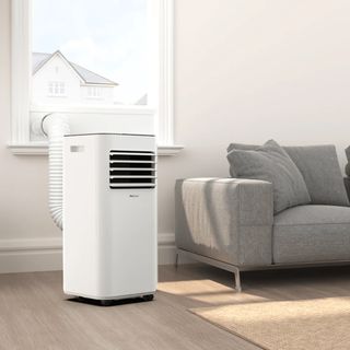 The ProBreeze portable air conditioner venting out of a window in a living room with a wooden floor and grey sofa
