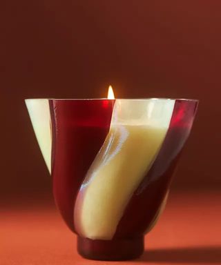 By Anthropologie Candy Twist Fruity Plum & Fir Balsam Glass Candle against a red background.