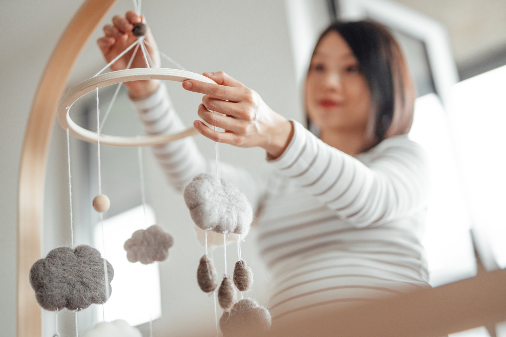 A pregnant woman installs a baby's mobile above a crib.