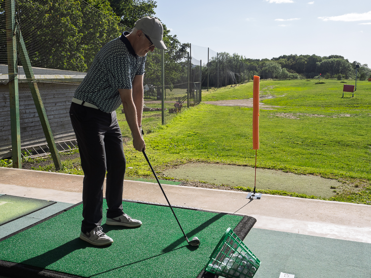 A male golfer on a driving range aiming at a stick