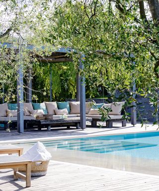 A pergola area featuring a large outdoor sofa next to a pool