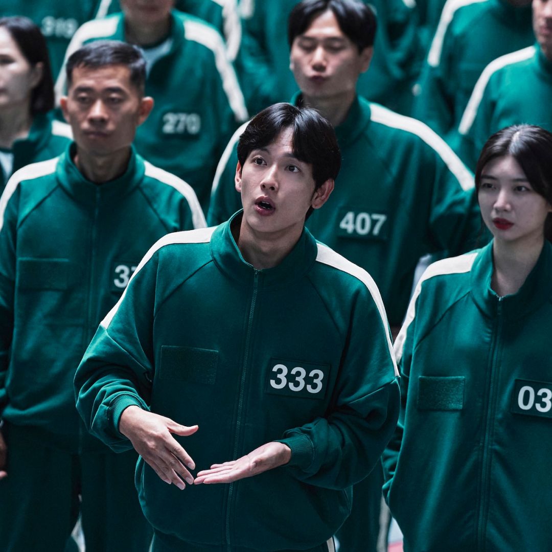 A group of people wearing identical green tracksuits with numbers printed on them, in &#039;Squid Game&#039; season 2.