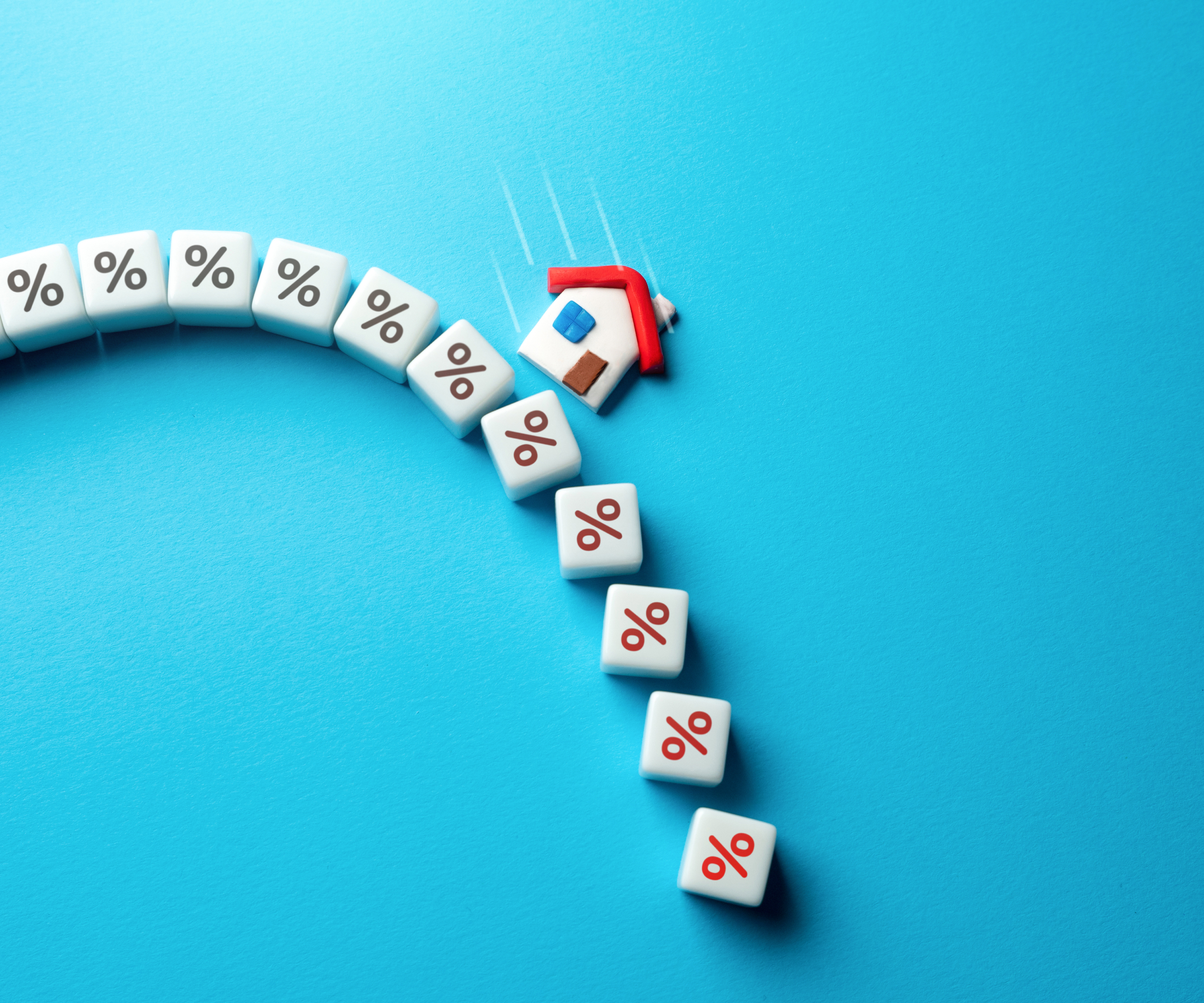 small plastic house on cubes with % sign placed in downward arc on blue background