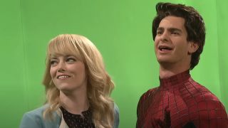 Emma Stone as Gwen and Andrew Garfield as Spider-Man standing in front of a green screen smiling on SNL.