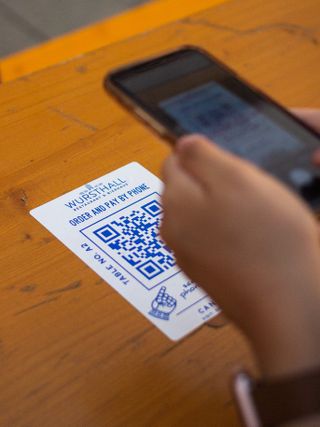 A person holding an iPhone over a QR code on a table