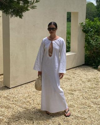 influencer Sasha Mei poses outside in a Marlies Grace white linen dress with flared sleeves and a large teardrop cutout on the chest