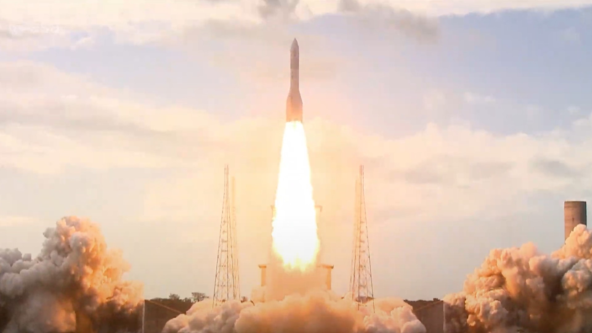 a large white rocket lifts off through a cloudy sky above a massive plume of fire and smoke