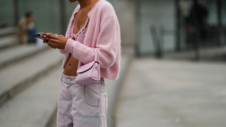 guest wears a pale pink wool cardigan, a pale pink shiny leather crocodile pattern handbag, high waist denim cargo denim large pants, a pink rhinestones checkered cut-out V-neck cropped tank-top, outside Ludovic de Saint Sernin, during Paris Fashion Week - Womenswear Spring Summer 2022, on October 03, 2021 in Paris, France