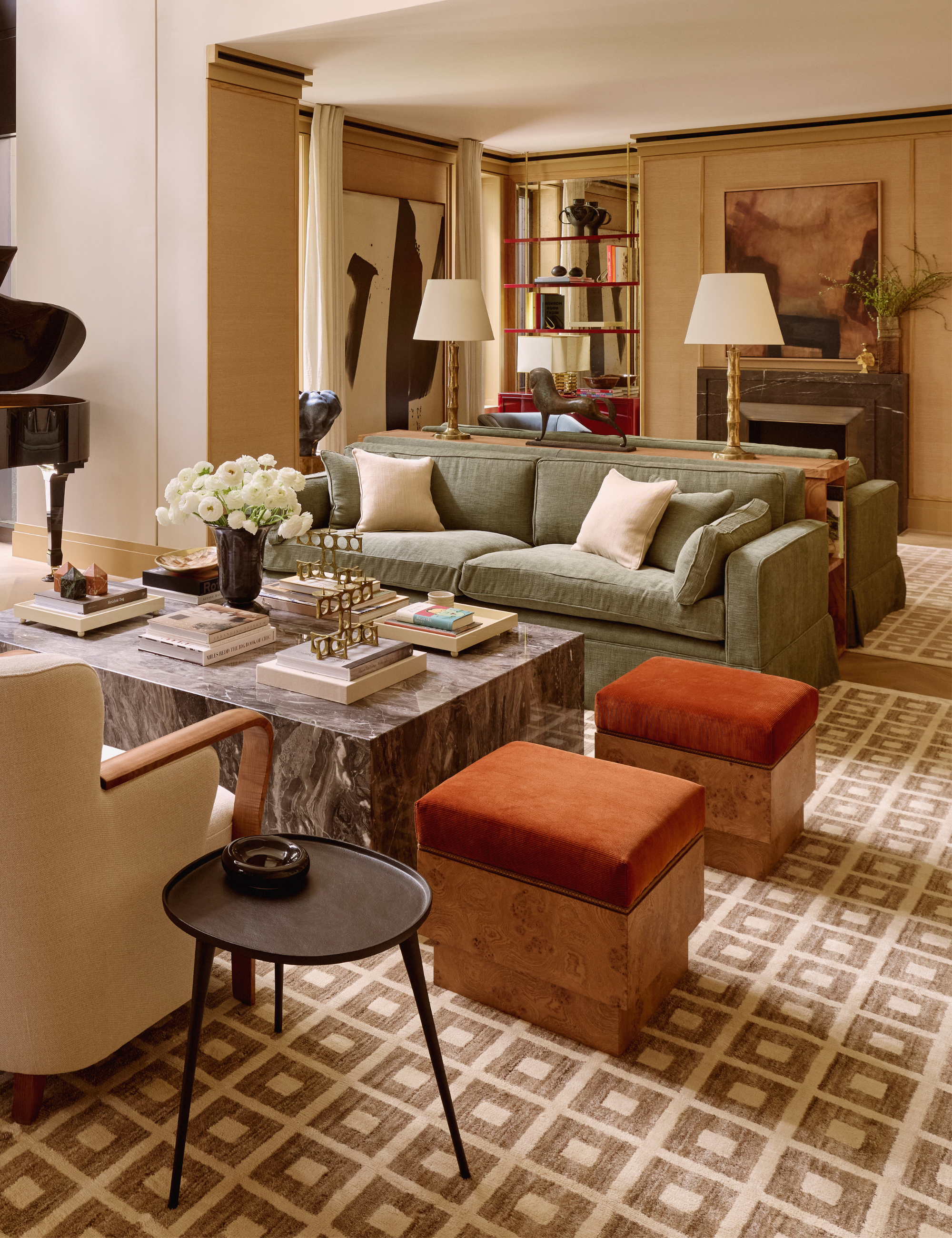 Collected living room area of rich patterns and textures, featuring a sleek marble coffee table, burl wood ottomans, moss green sofas, and oversized linen-shaded table lamps.