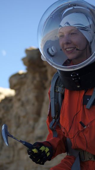 a woman in a spacesuit holds a pickaxe