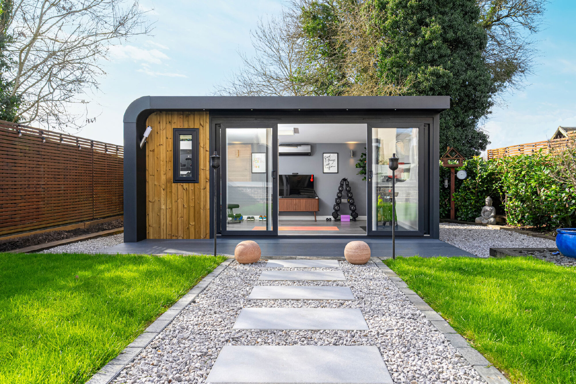 A gravel path with pavers leading up to a modern outbuilding studio shed in a garden