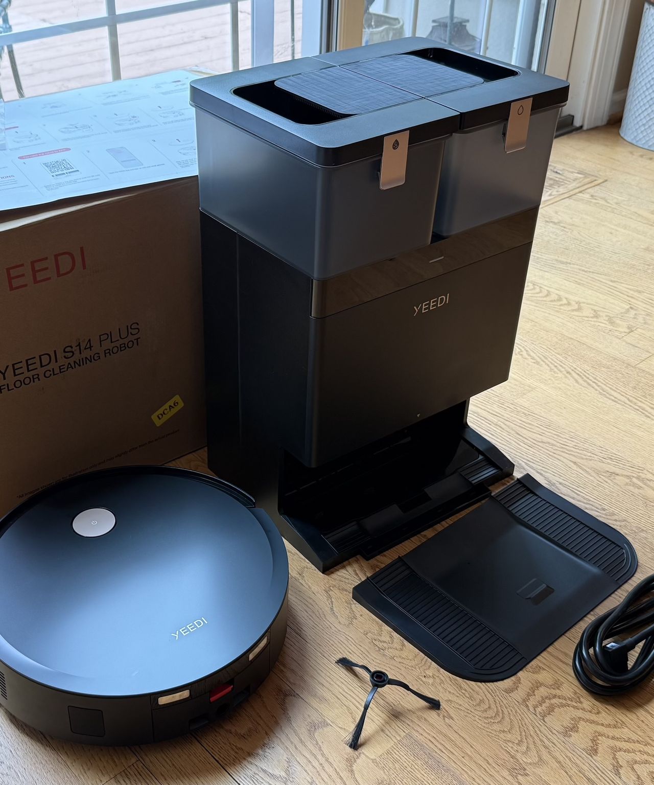 Yeedi S14 Plus robot vacuum, cleaning station, parts and packaging on wooden floor in James Holland's home.