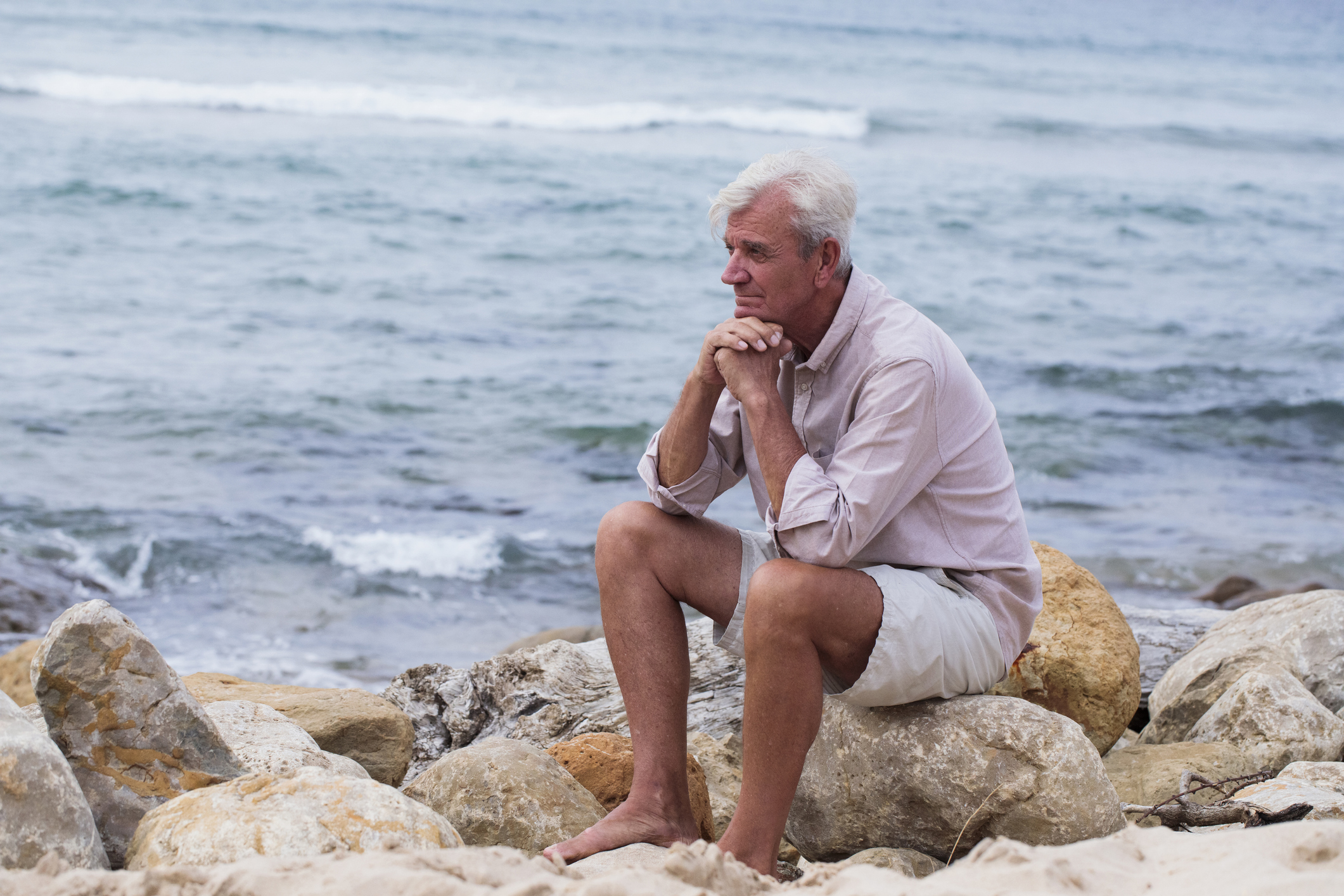 A senior man sits alone on a beach.