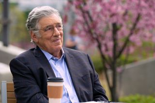 Elliott Gould as Legal Siegel, sitting at an outdoor table with a takeout coffee cup, in episode 209 of The Lincoln Lawyer.