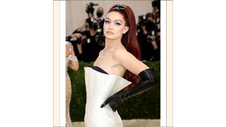 Gigi Hadid with red hair and wearing a white dress and black gloves as she attends The 2021 Met Gala Celebrating In America: A Lexicon Of Fashion at Metropolitan Museum of Art on September 13, 2021 in New York City.