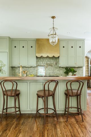 a green kitchen with a brass scallop hood
