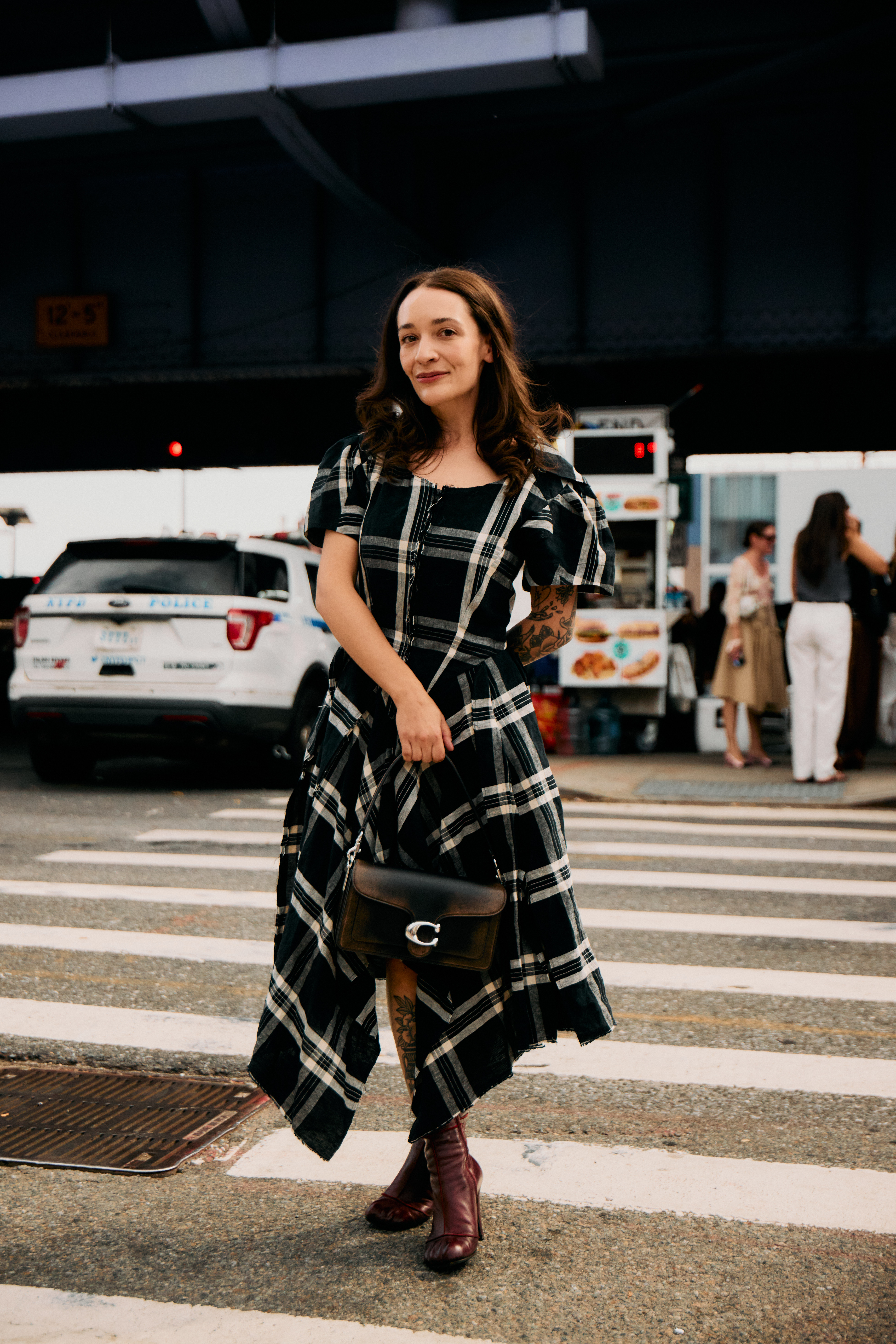 Woman in plaid midi dress, burgundy boots, and Coach bag.