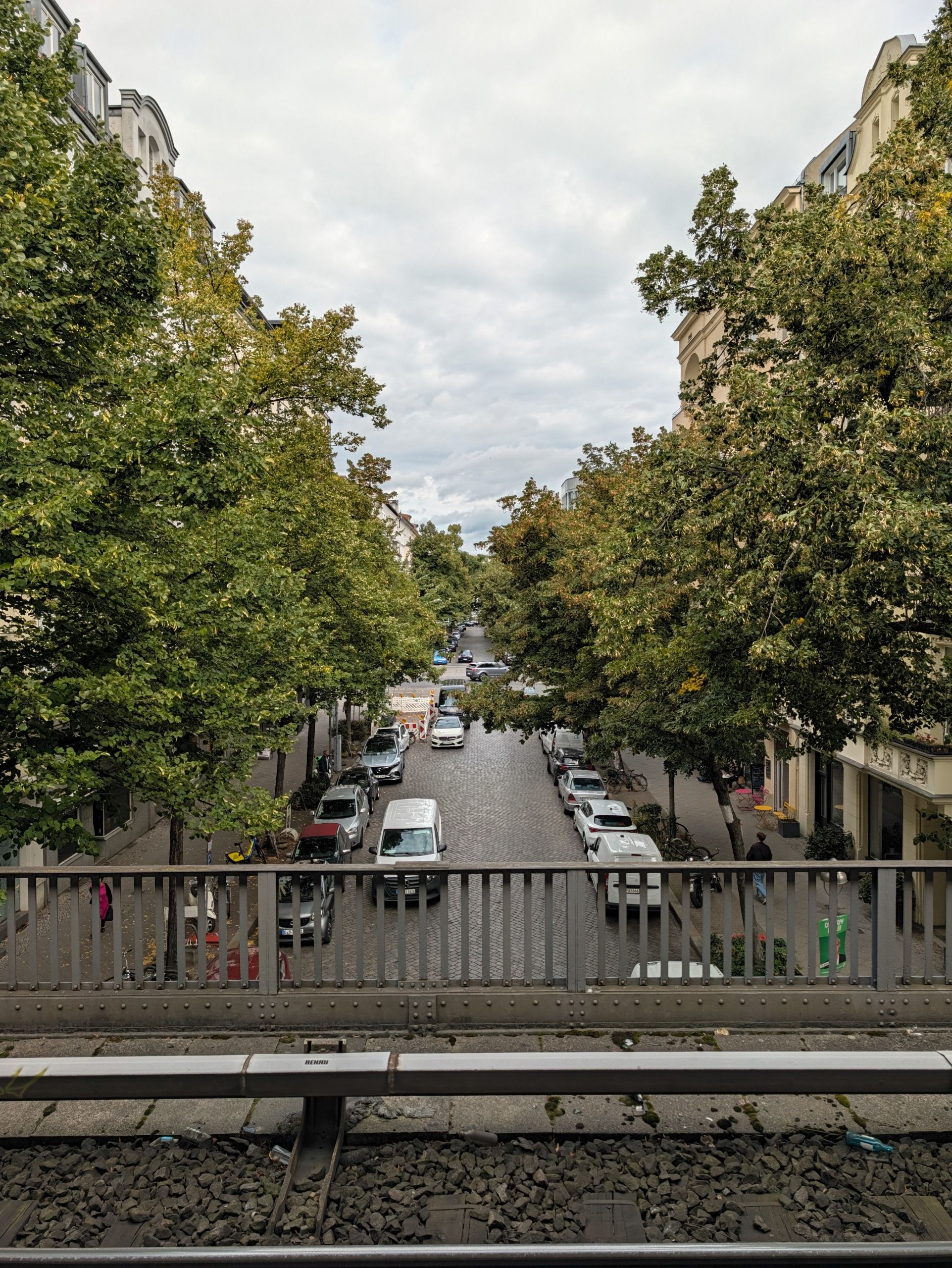 Tree-lined residential street viewed from an elevated railway line in Berlin.