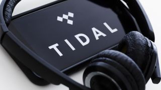A phone running Tidal with a pair of black headphones