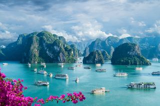 A landscape view of Halong Bay, Vietnam, with several small cruise ships and towering cliffs.