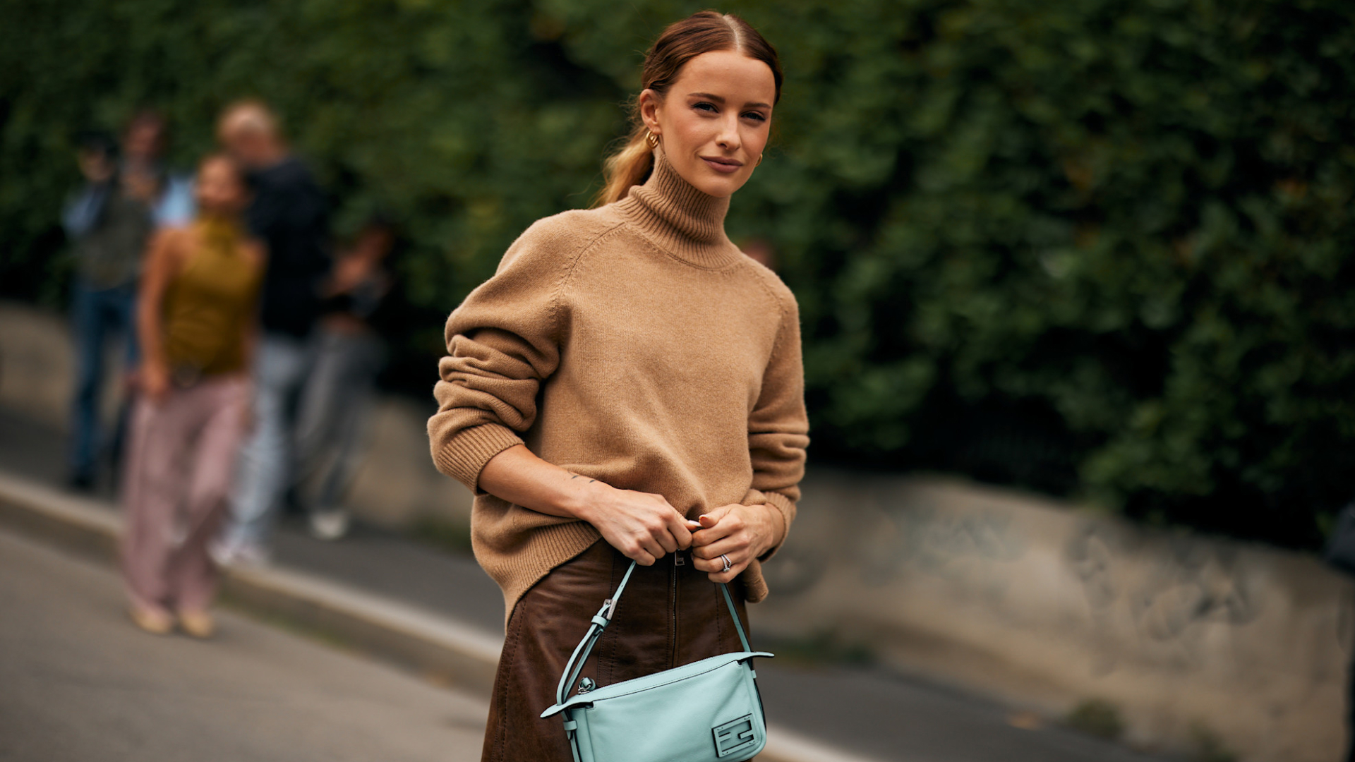 fashion week attendee wearing a ponytail hairstyle, tan turtleneck, and light blue bag