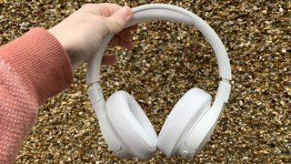 Someone holding the jbl tune 750btnc over-ear headphones against a brown, earthy surface
