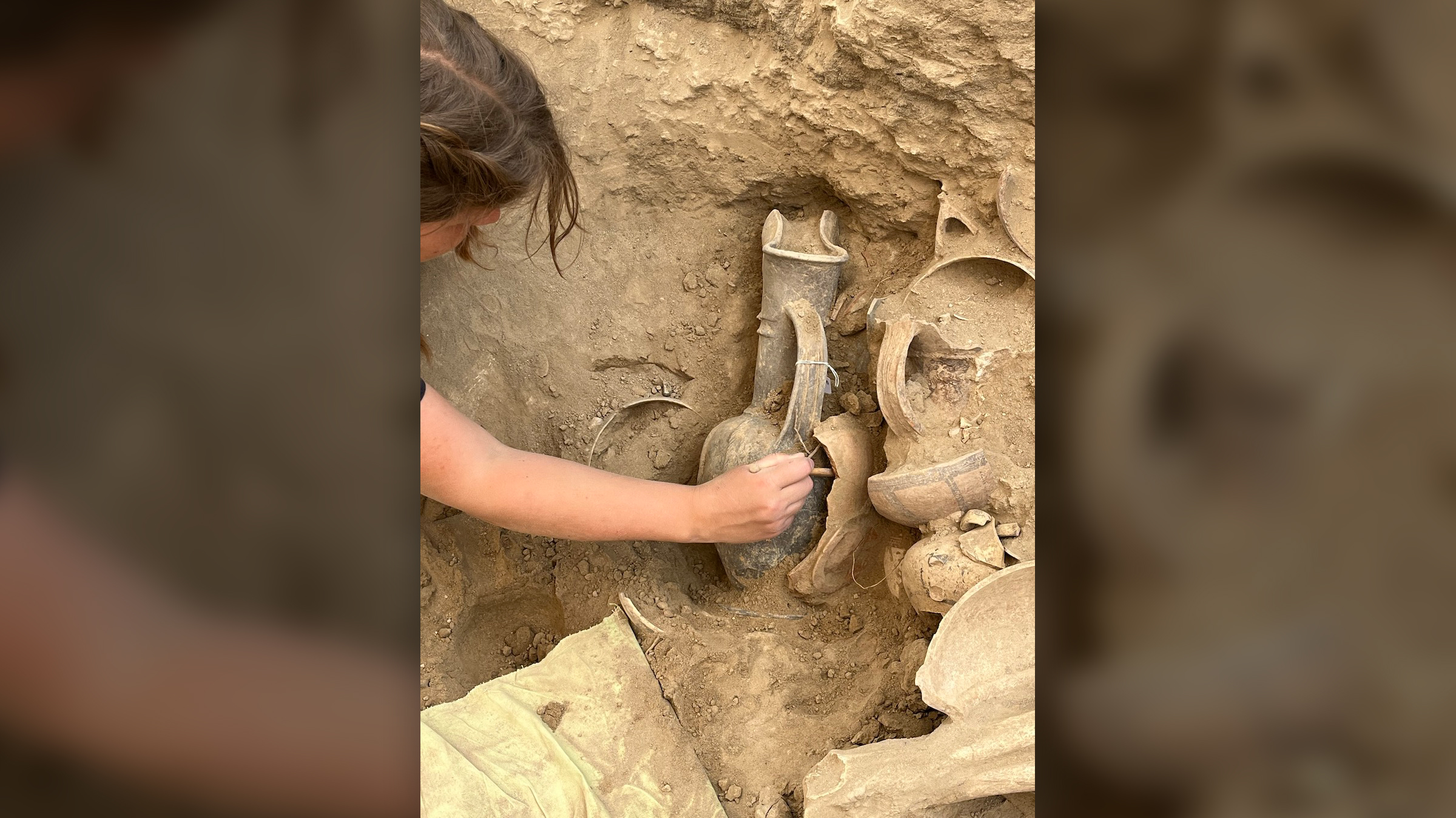 Una investigadora alcanza una jarra enterrada en la tierra.