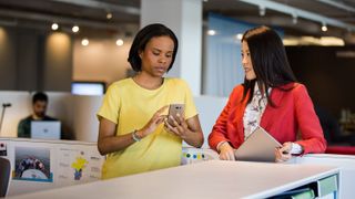 Two women discuss work while one looks at her Android smartphone