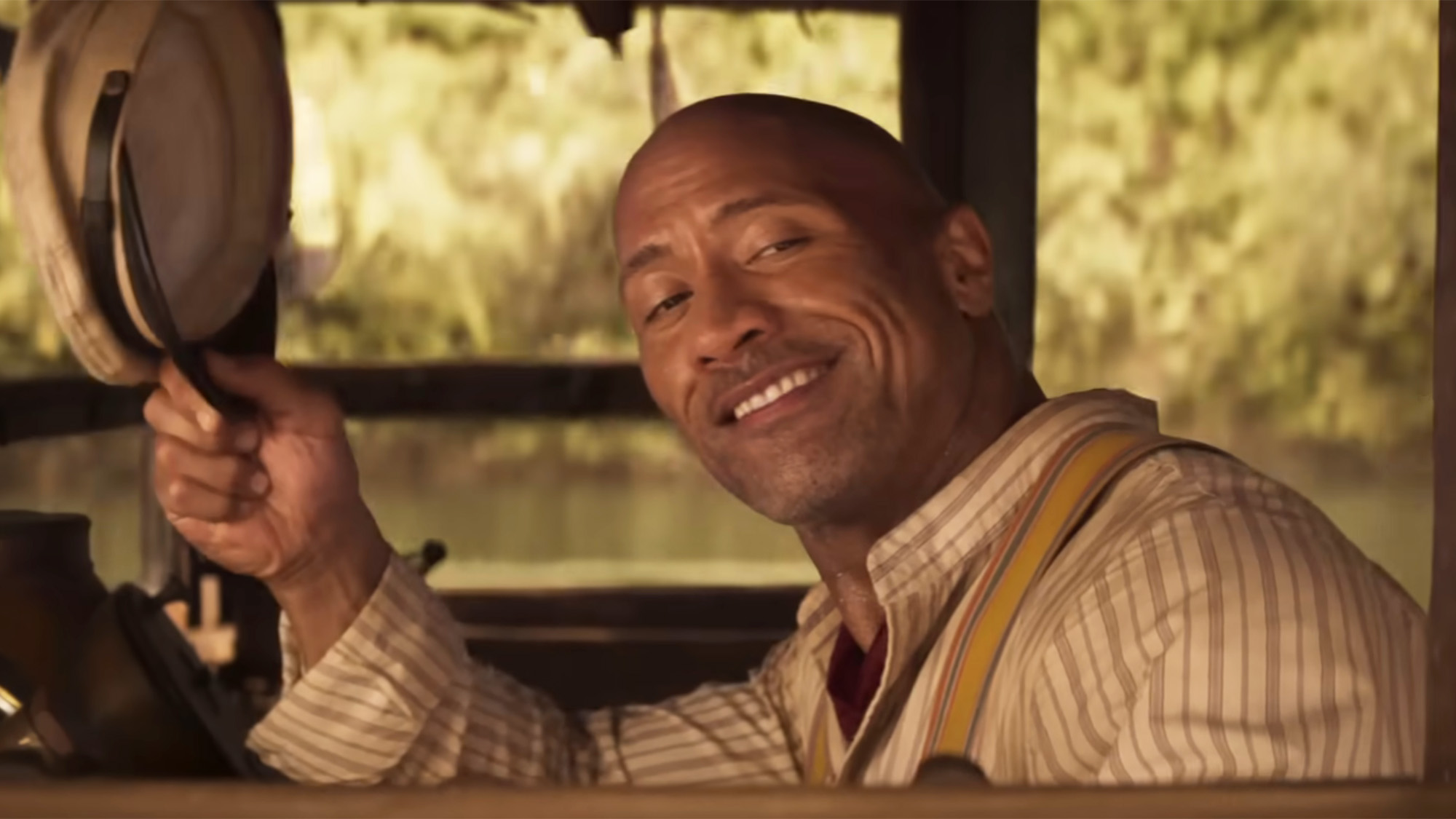 Dwayne Johnson doffing his hat while wearing suspenders on a boat in Jungle Cruise 2022.