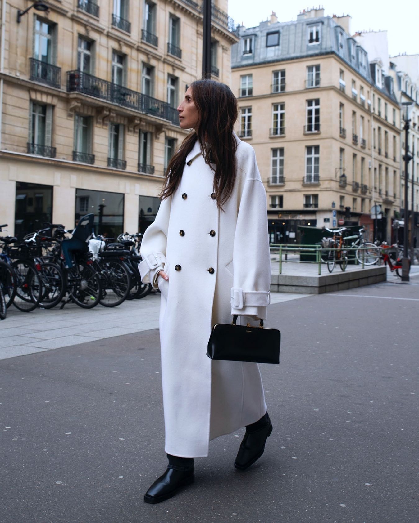 @chloe_harrouche wearing a double-breasted coat with boots and an east-west bag.