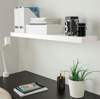 A home office with black desk, indoor houseplant and white floating shelf on wall