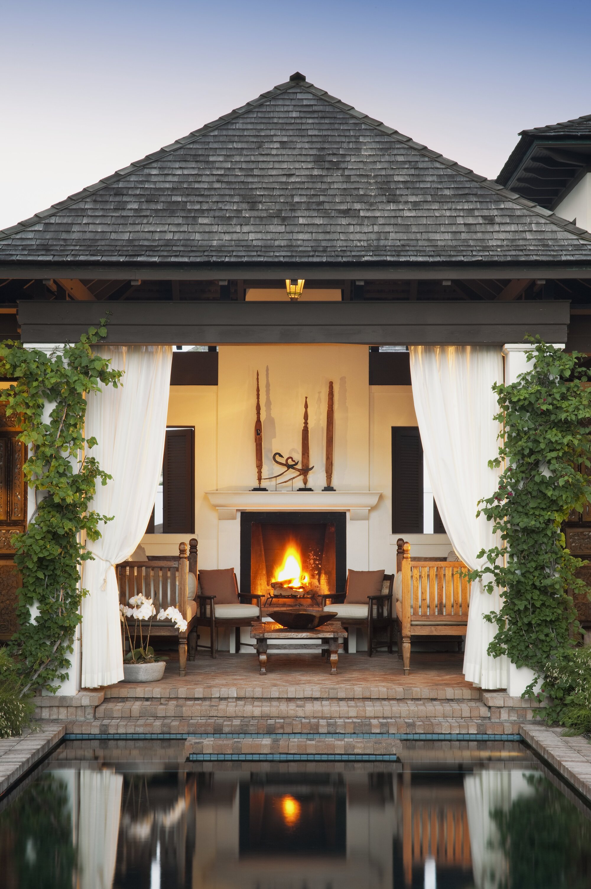 An outdoor porch area with brick steps, a fireplace, garden furniture, and white curtains tied back