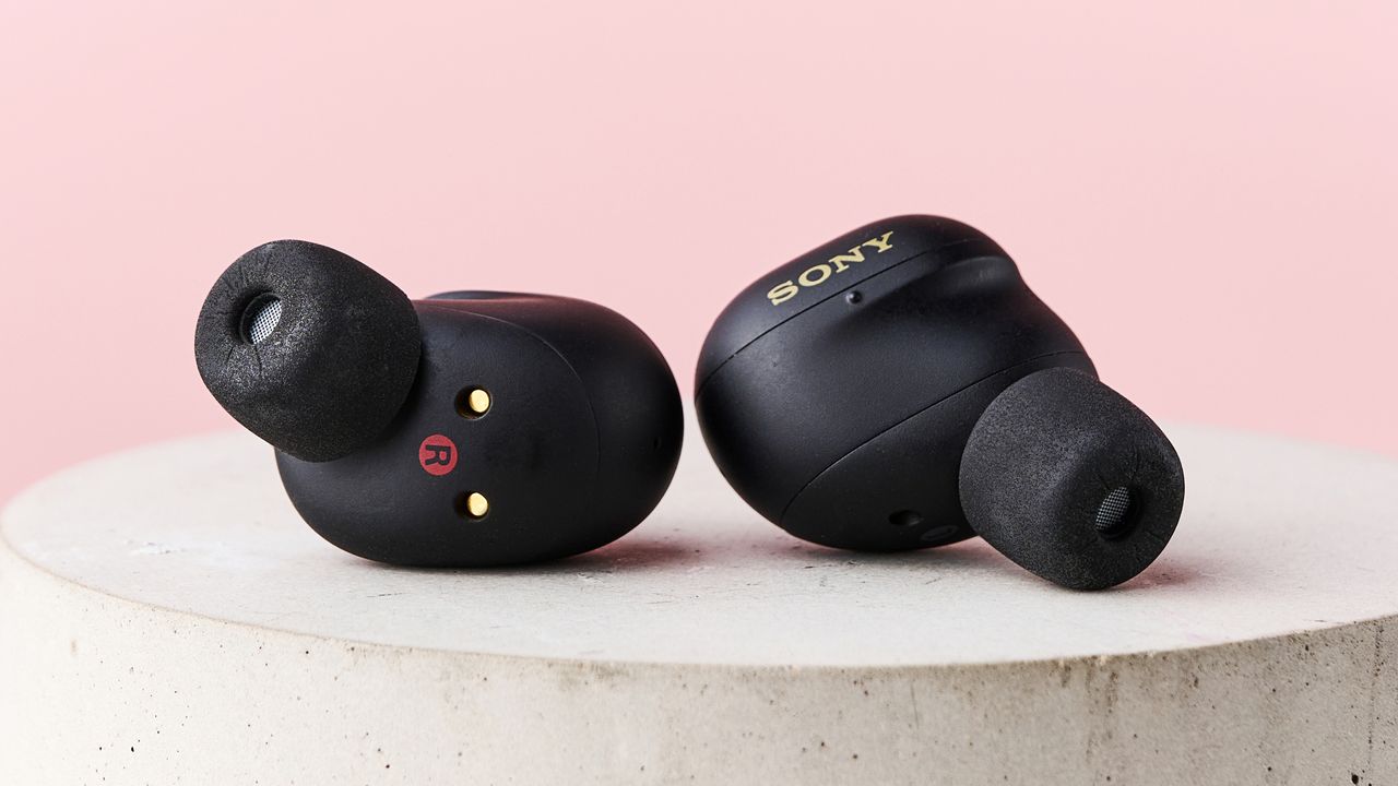 The Sony WF-1000XM6 lying loose on top of a stone pillar in front of a pink background.