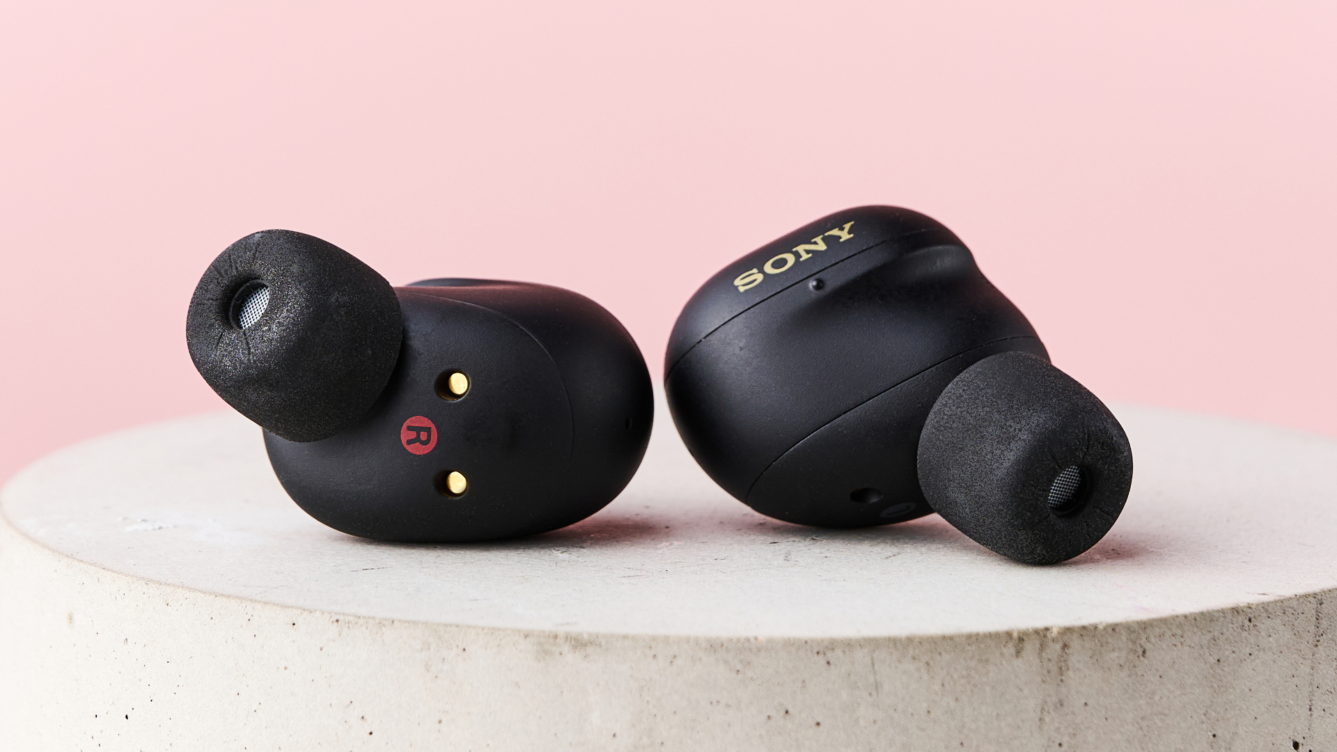 The Sony WF-1000XM6 lying loose on top of a stone pillar in front of a pink background.