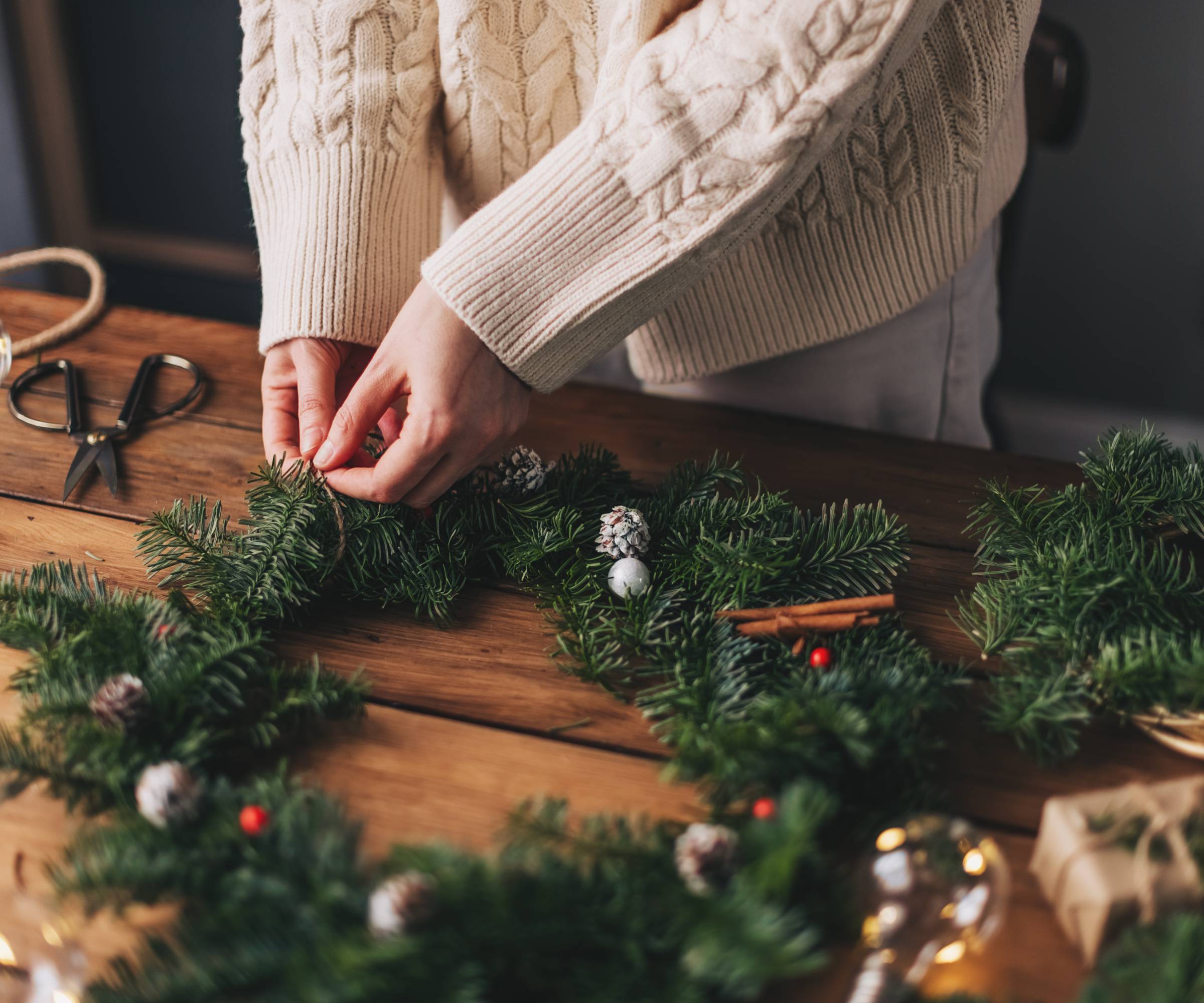 A woman&#039;s hands securing evergreen boughs to a wreath